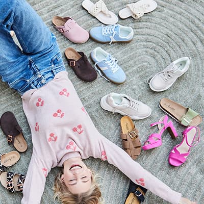 Person liegt auf Teppich, umgeben von verschiedenen Schuhmodellen