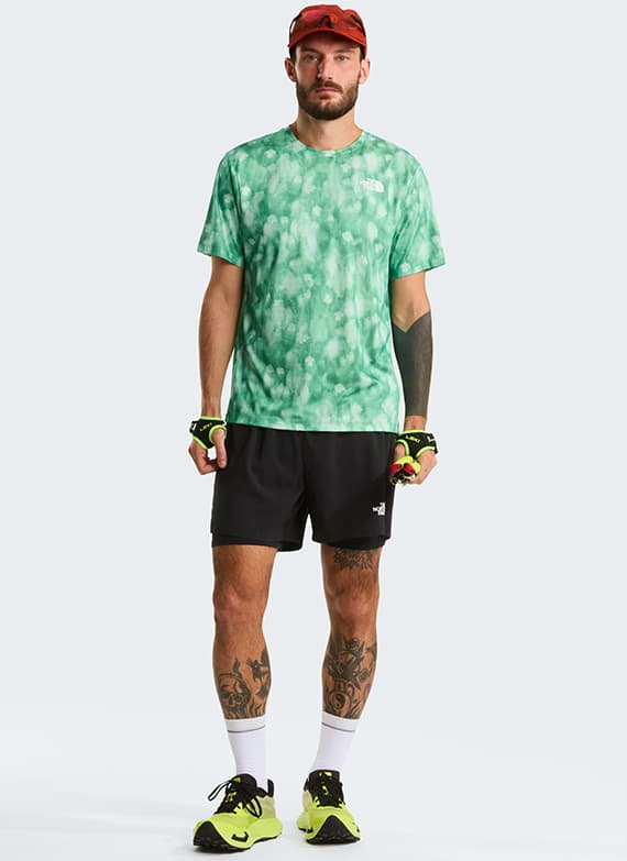 Mann trägt grünes T-Shirt, schwarze Shorts, Laufschuhe und Handschuhe. Gesicht ist unscharf.