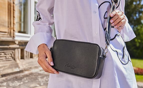 Frau hält eine kleine schwarze Umhängetasche vor ihrem weißen Hemd.