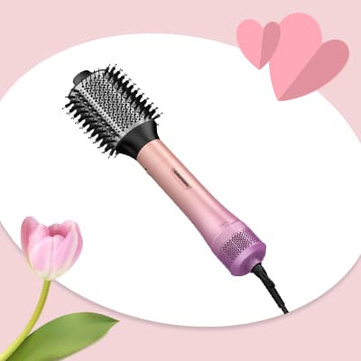 Rosa Heißluftbürste mit Kabel vor hellem Hintergrund, daneben rosa Tulpe und zwei stilisierte Herzen