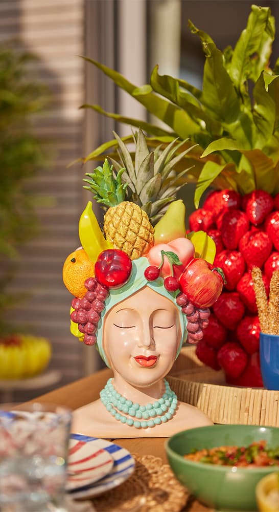 Deko-Büste mit bunter Obstkrone und Perlenkette steht als Tischmitte auf sommerlich gedeckter Tafel