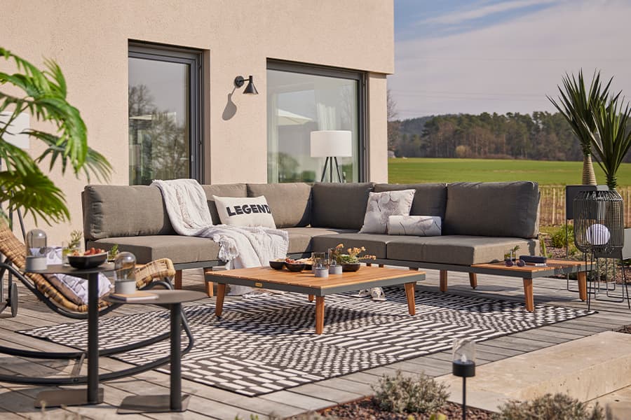 LEGEND-Kissen auf großer Ecklounge, mit Decke und Kissen dekoriert, davor niedrige Tische auf gemustertem Outdoor-Teppich