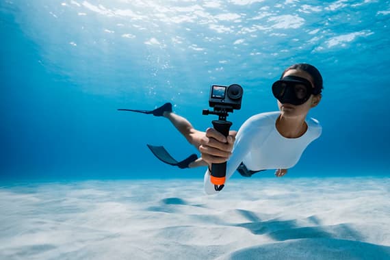 Person mit Flossen filmt unter Wasser mit Actionkamera über hellem Sandboden
