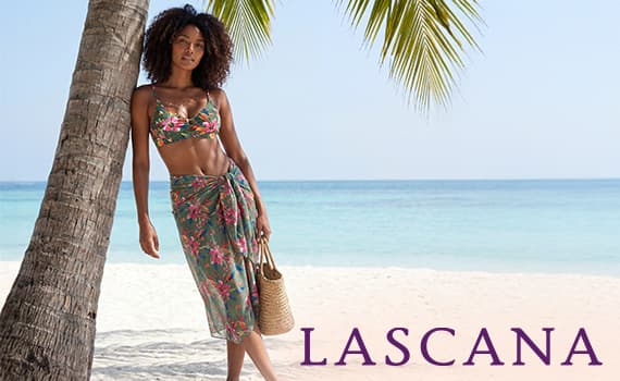 LASCANA – Frau im gemusterten Bikini mit Pareo lehnt an Palme am Strand und hält eine Basttasche