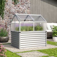 Kleines Hochbeet-Gewächshaus im Garten, gefüllt mit grünen Pflanzen vor Steinmauer und Terrasse