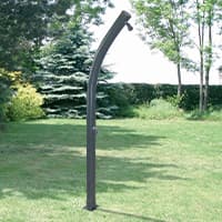 Gebogene Gartendusche mit Duschkopf steht frei auf Rasenfläche vor Bäumen und Hecke