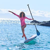 Frau in pinkem Einteiler balanciert mit Paddel auf einem Stand-up-Paddle-Board auf dem Meer