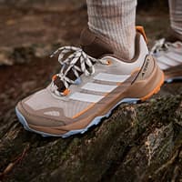 Outdoor-Sneaker mit hellen Streifen, getragen von Person auf einem moosigen Baumstamm im Wald