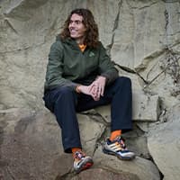 Person in Outdoorjacke und Hose sitzt auf Felsen, bunte Wanderschuhe und orange Socken deutlich sichtbar
