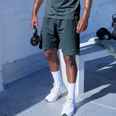 Mann in Sportoutfit steht mit Hantel in der Hand auf Terrasse neben Bank mit Hanteln