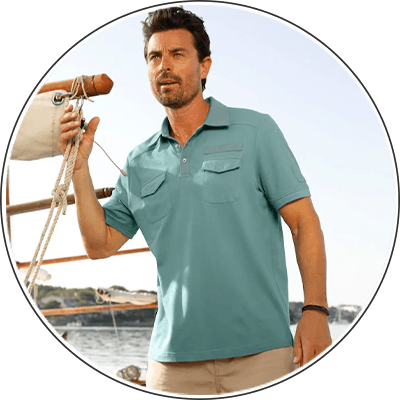Mann in türkisgrünem Poloshirt steht auf einem Boot und hält ein Tau, im Hintergrund Wasser und Uferlandschaft