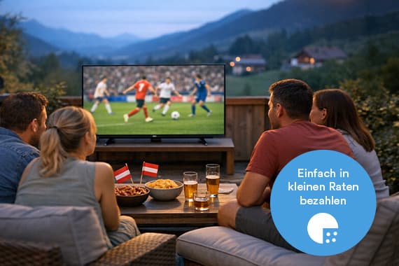 Einfach in kleinen Raten bezahlen – vier Personen schauen abends auf der Terrasse Fußball auf einem großen Fernseher