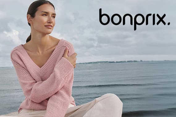 bonprix Logo – Frau im rosa Pullover sitzt am Meer und blickt zur Seite