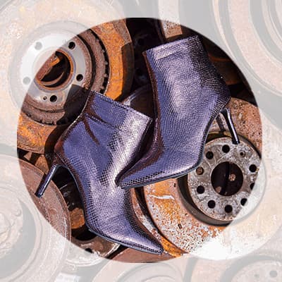 Glänzende Stiefeletten mit Absatz liegen überkreuz auf rostigen Metallscheiben