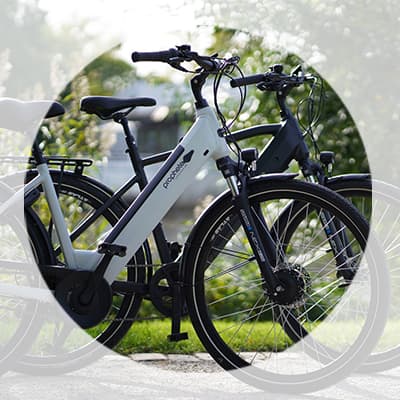 Zwei moderne E-Bikes nebeneinander auf einem Weg im Grünen, Fokus auf das vordere helle Rad