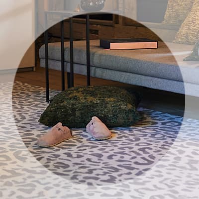 Wohnzimmer mit Sofa, Beistelltisch, gemustertem Teppich, großem Kissen und Hausschuhen auf dem Boden