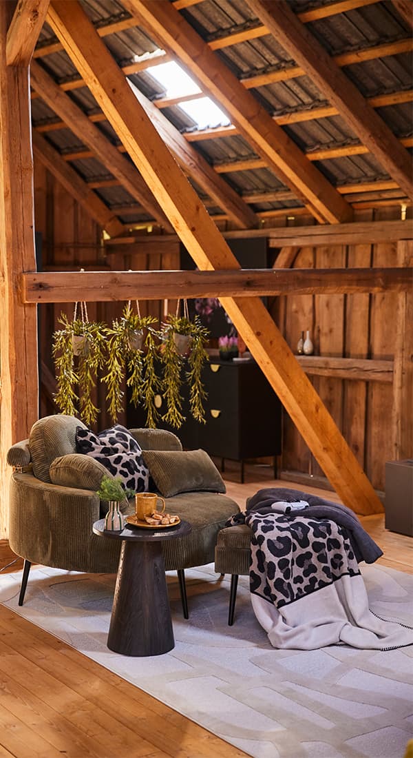 Sessel mit Hocker unter Dachbalken, Decke mit Leopardenmuster, Beistelltisch mit Tee und Gebäck, hängende Pflanzen im Hintergrund