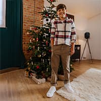 Junge steht lächelnd vor geschmücktem Weihnachtsbaum in gemütlichem Wohnzimmer