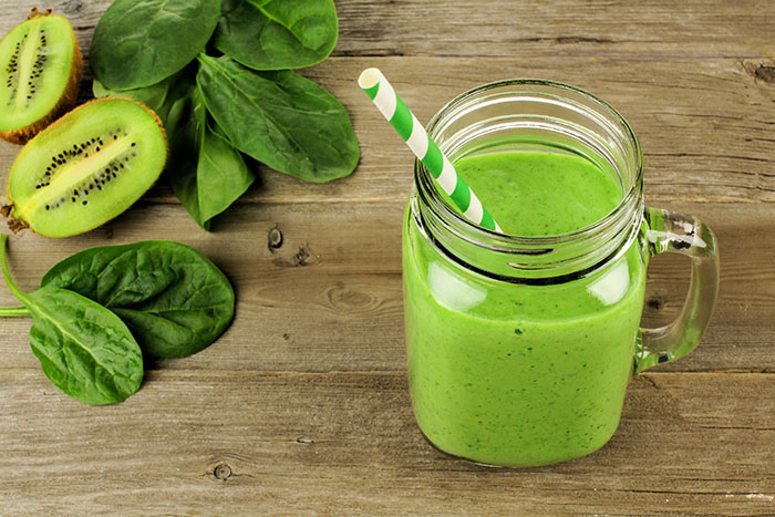 Healthy green smoothie with spinach and kiwi in a jar mug on wood, downward view