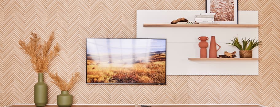 Wand mit Muster, Wandregale mit Dekorationen, TV zeigt Landschaftsbild, Vasen mit Trockenblumen und grünen Pflanzen