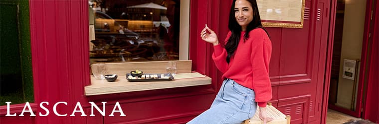 LASCANA – Frau in rotem Pullover und blauer Jeans sitzt vor einem roten Café und hält eine Einkaufstasche