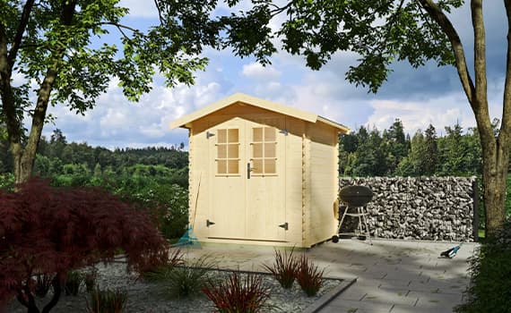 Holz-Gartenhaus mit Fenstern auf gepflastertem Platz, umgeben von Bäumen und Pflanzen, Grill daneben