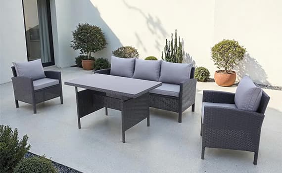 Gartenmöbel-Set mit zwei Sesseln, einem Sofa und einem Tisch auf einer Terrasse mit Pflanzen im Hintergrund