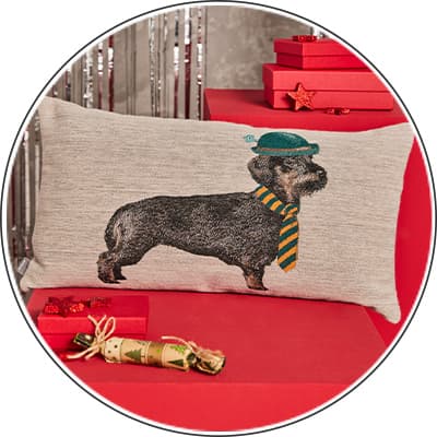 Zierkissen mit Hundemotiv – Hund mit grünem Hut und gestreiftem Schal, auf rotem Geschenkstapel mit dekorierten Geschenken