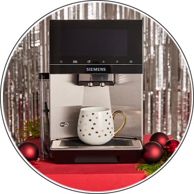 Siemens Kaffeevollautomat – weiße Tasse mit goldenen Sternen auf rotem Tisch vor festlicher silberner Dekoration