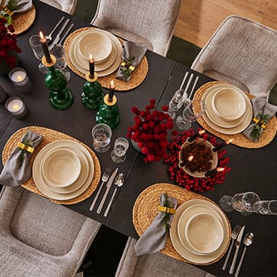 Festlich gedeckter Tisch mit Teller-Set, Kerzen, Besteck, Gläsern und roten Dekorationsblumen