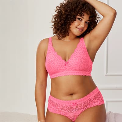 Frau in pinker Spitzenunterwäsche steht mit Hand im Haar und zeigt Körperschmuck.